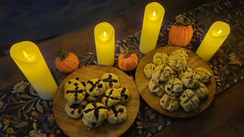 Four lit candles on a table with two plates of small biscuits and small pumpkins.